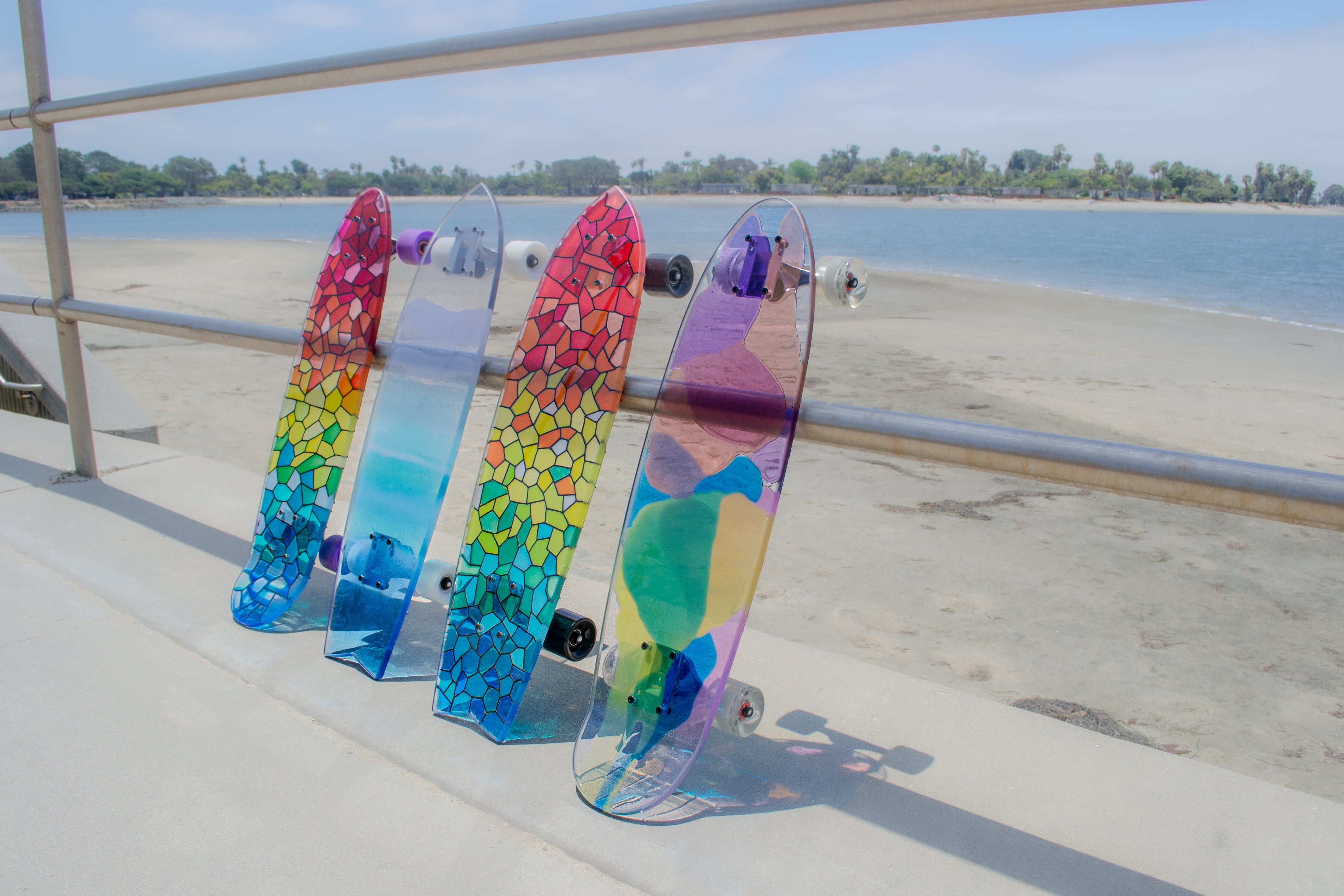 Four colorful, see through stained glass skateboards in rainbow and ocean resin casting colorful shadows.