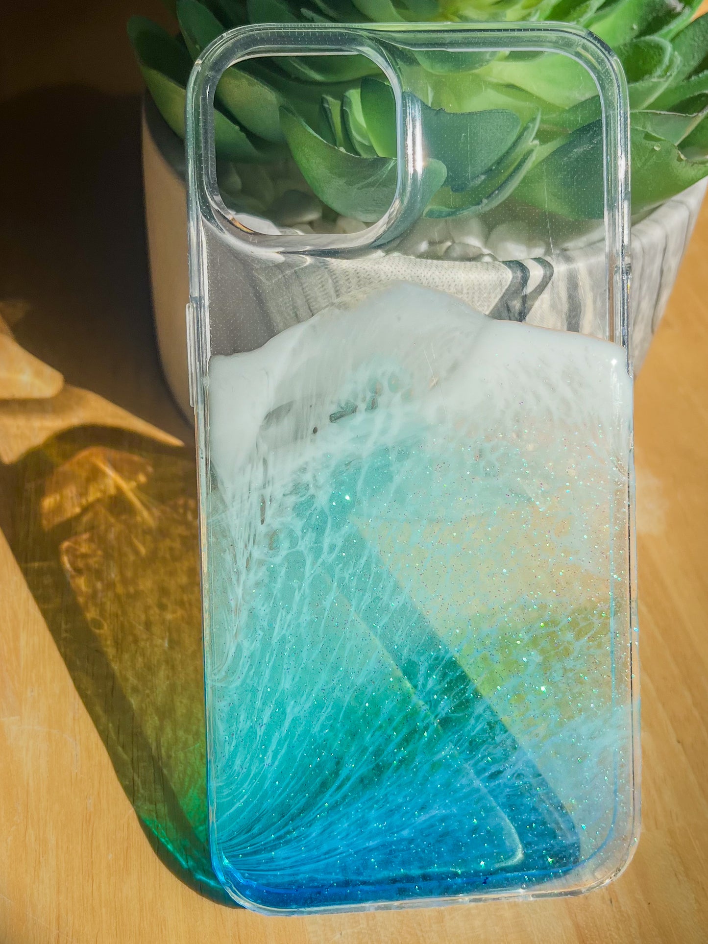 Blue resin ocean wave iPhone case casting colorful shadow in sunlight.