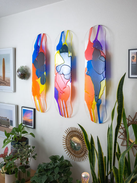 Three piece see-through stained glass skateboard deck wall art with red, orange, yellow, blue and purple resin layers.