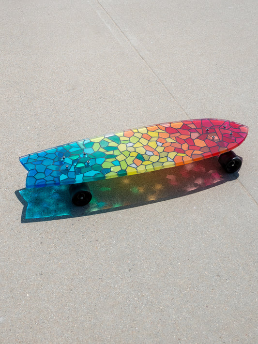 See-through rainbow stained glass skateboard with colorful shadow.