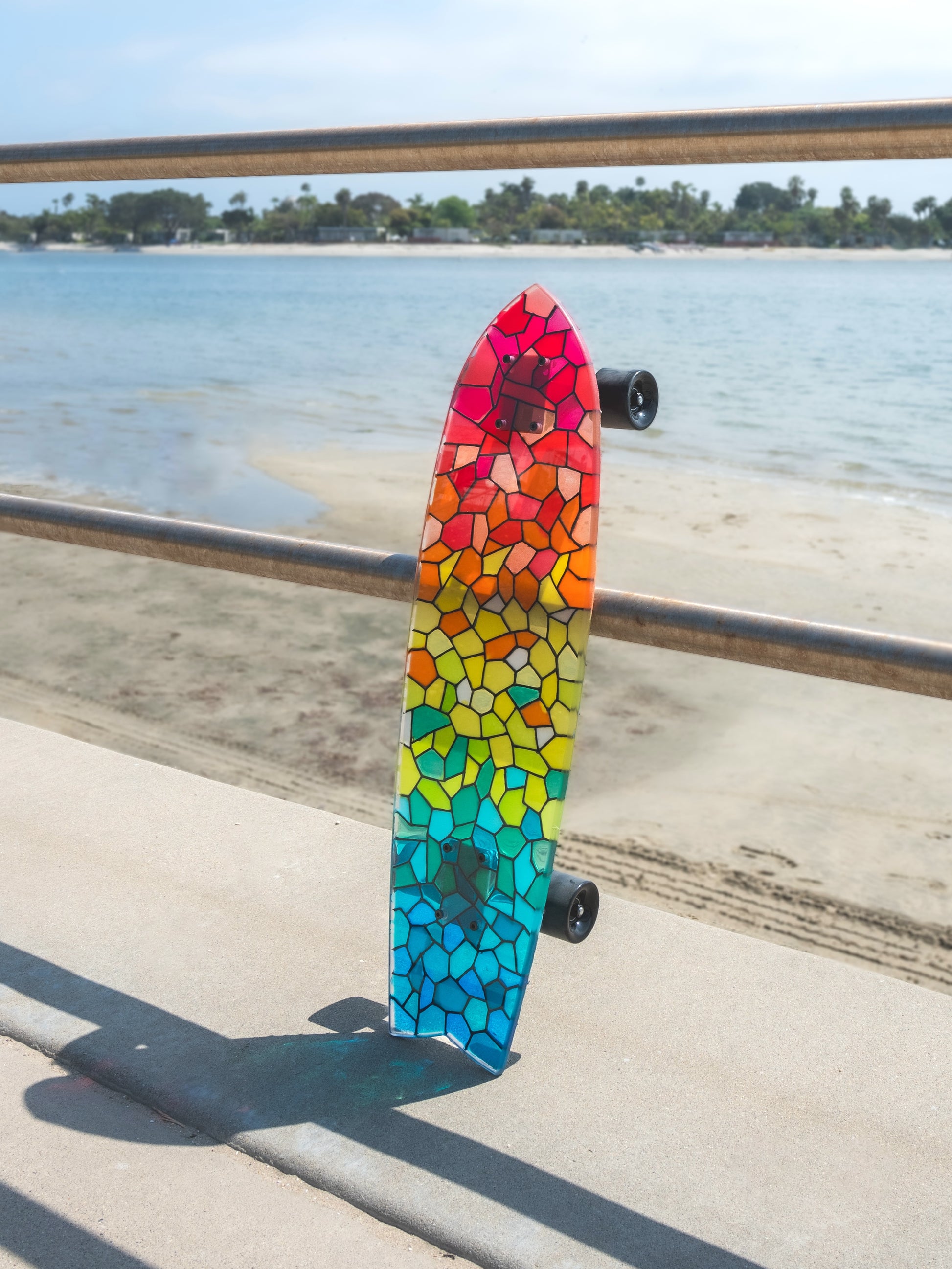 See-through rainbow stained glass skateboard with colorful shadow.