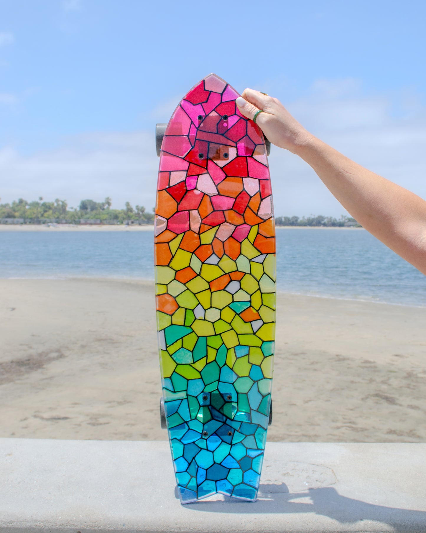 See-through rainbow stained glass skateboard with colorful shadow.