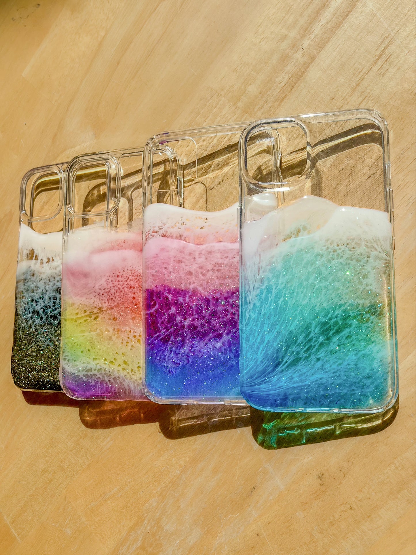 Handcrafted resin iPhone cases: vibrant rainbow, deep black, purple/pink, blue ocean designs. Modern, unique, durable art.