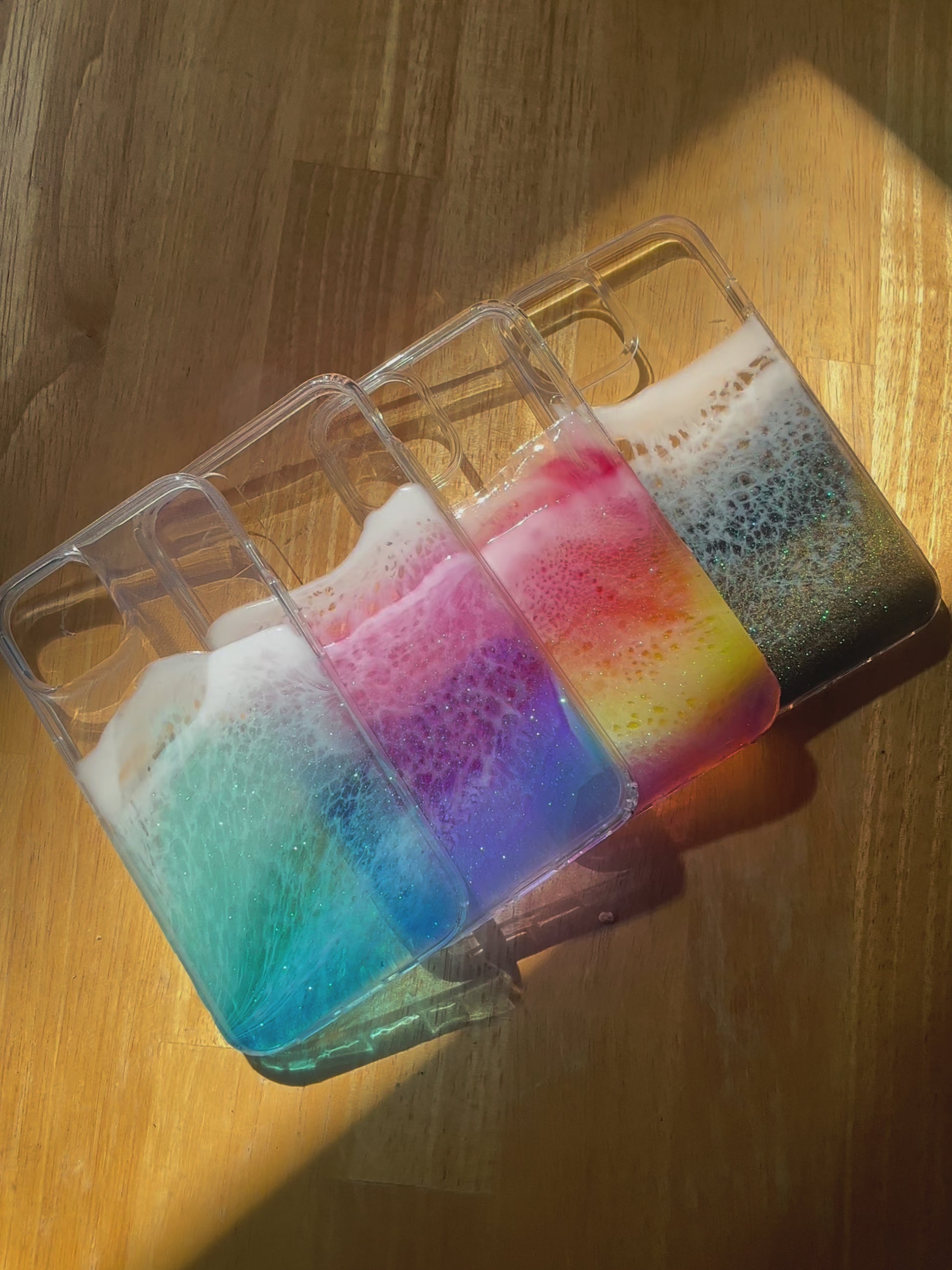 Handcrafted resin ocean iPhone cases in vibrant rainbow, black, purple/pink, blue.