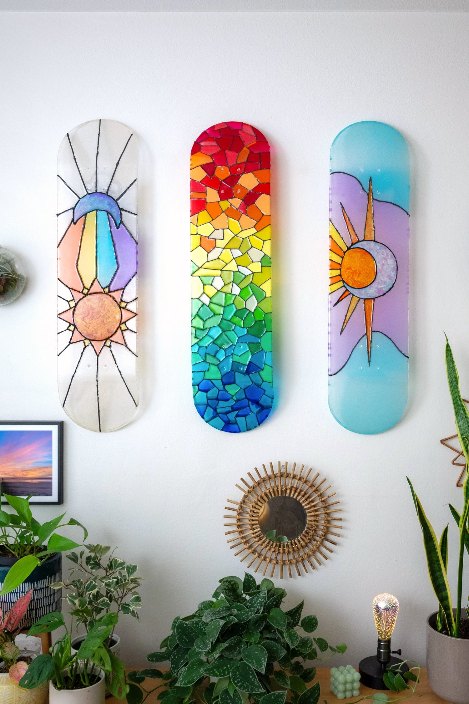 Three stained glass style pieces of skateboard wall art hanging with colorful shadows.