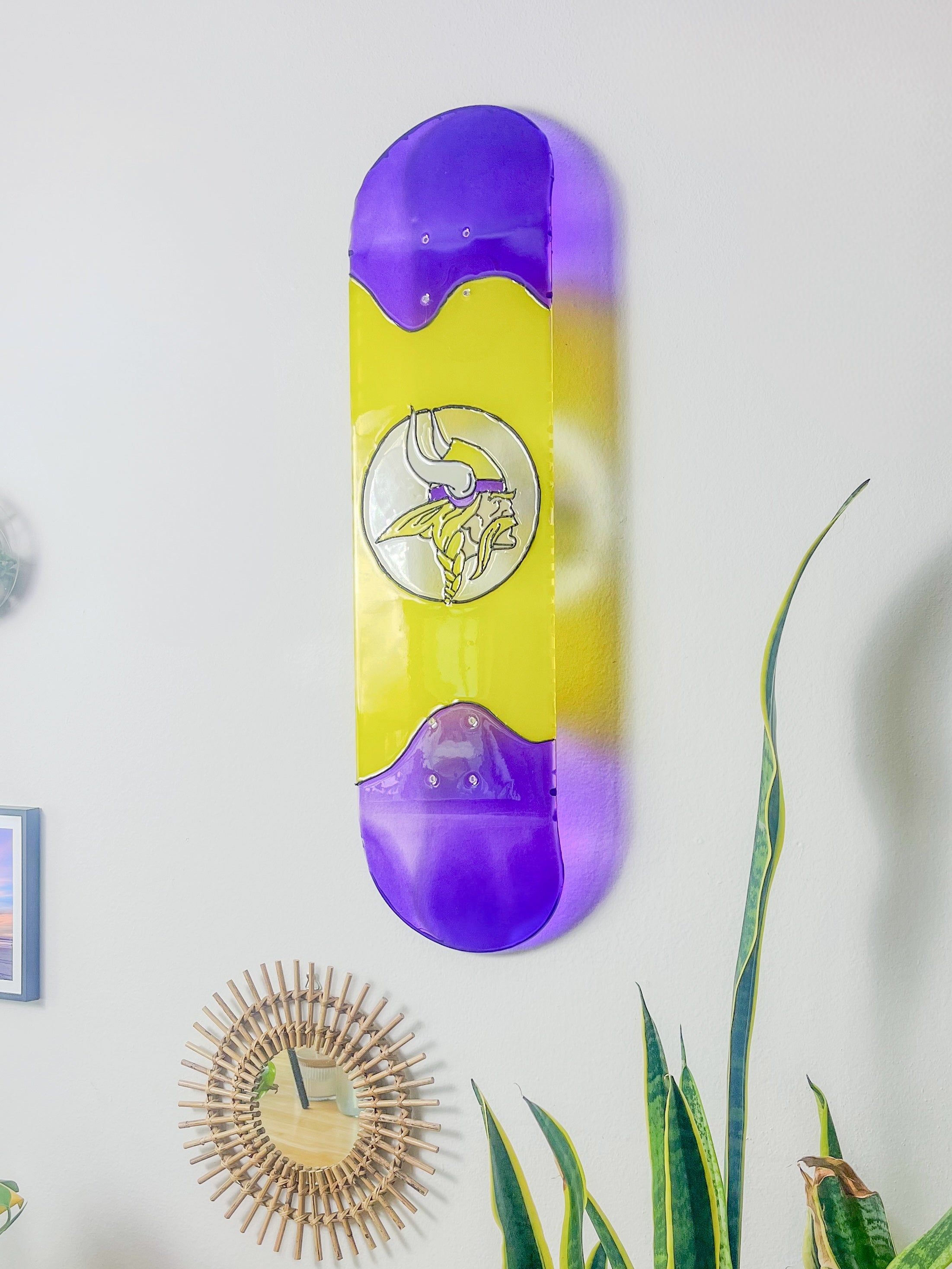 Custom stained glass skateboard deck with personalized logo casting colorful shadow on wall. 