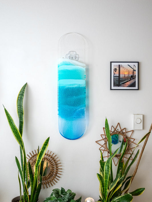 See-through blue resin ocean skateboard deck artwork casting colorful shadow on wall. 