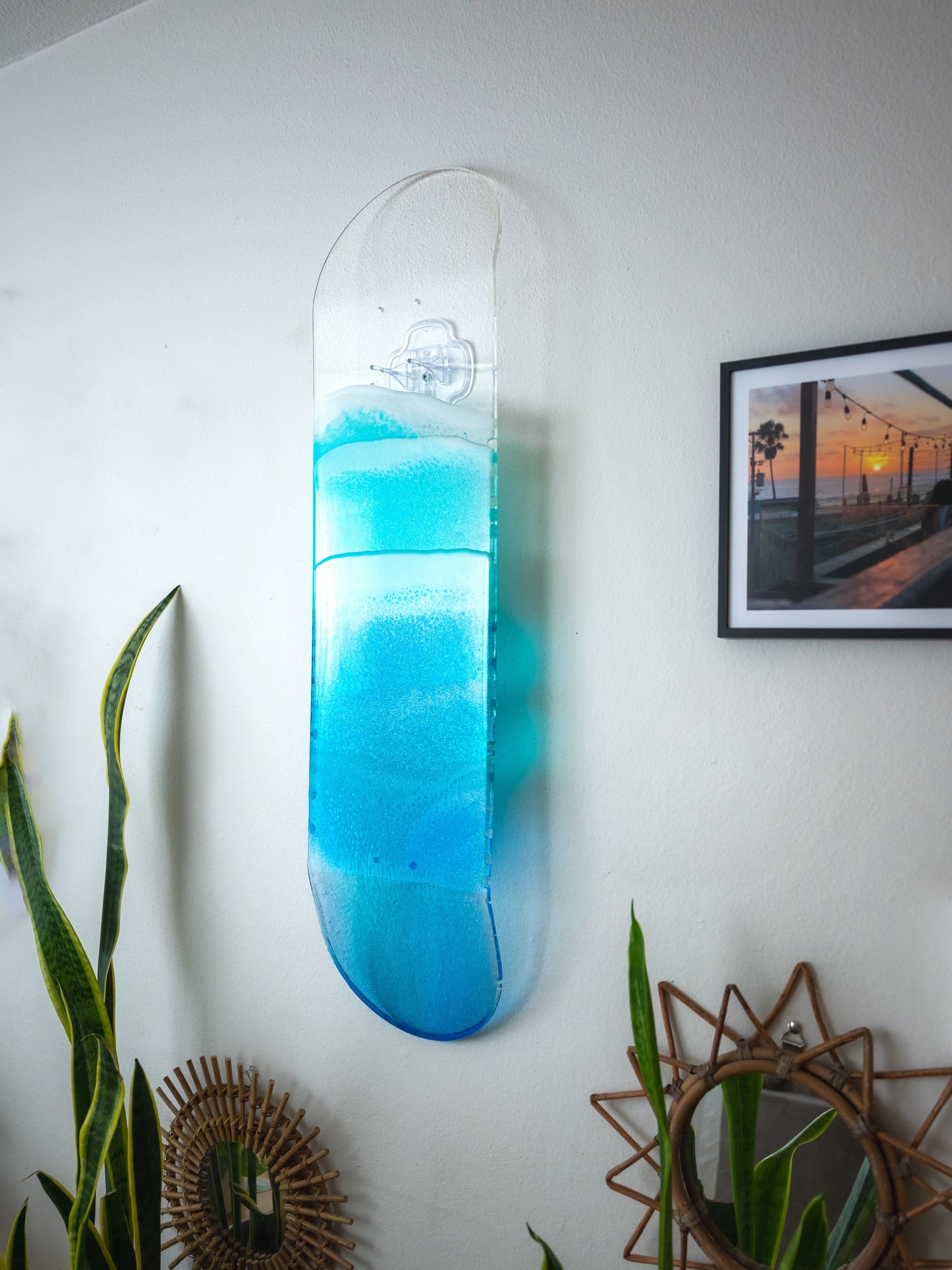 See-through blue resin ocean skateboard deck artwork casting colorful shadow on wall. 