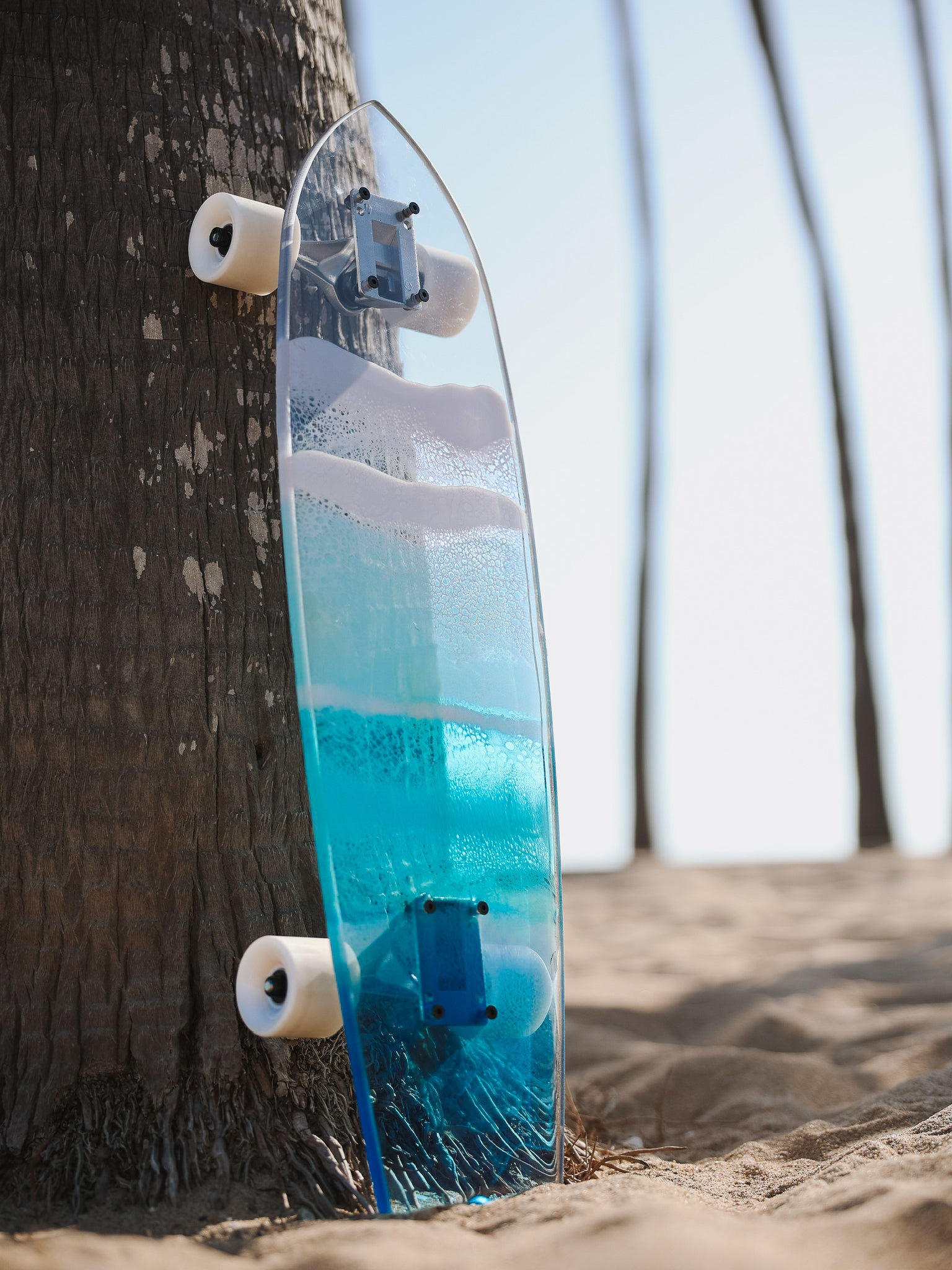 Blue, see-through resin ocean wave skateboard deck with fishtail casting colorful shadow.