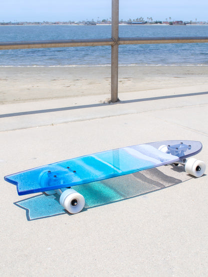 Blue, see-through resin ocean wave skateboard deck with fishtail casting colorful shadow.