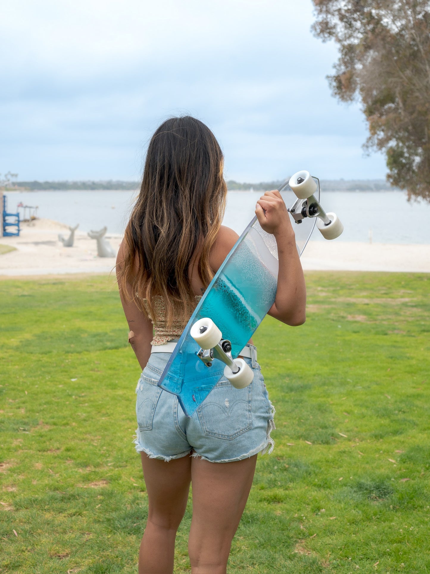 Blue, see-through resin ocean wave skateboard deck with fishtail casting colorful shadow.