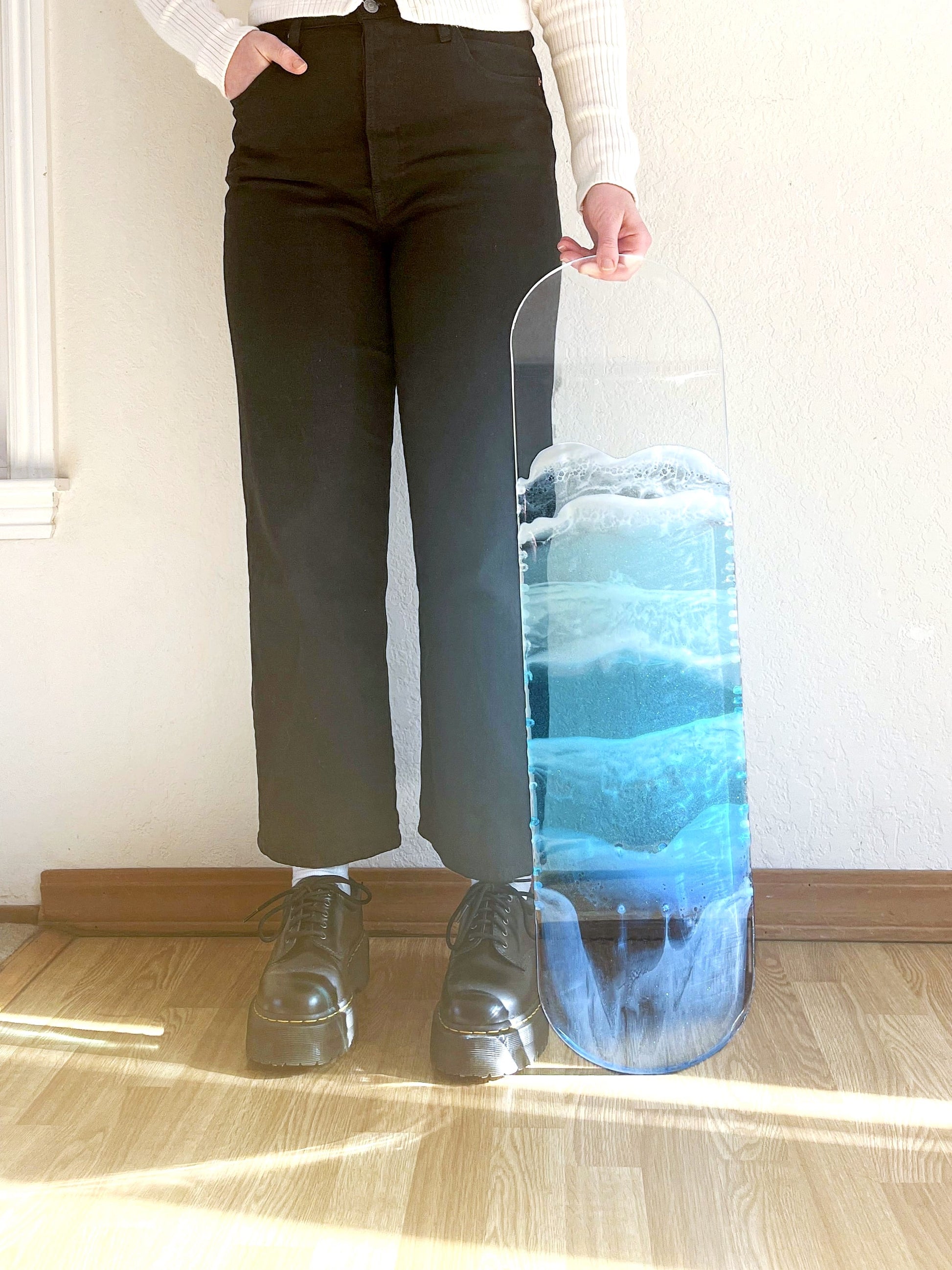 Woman standing next to see-through, blue resin ocean skateboard art.