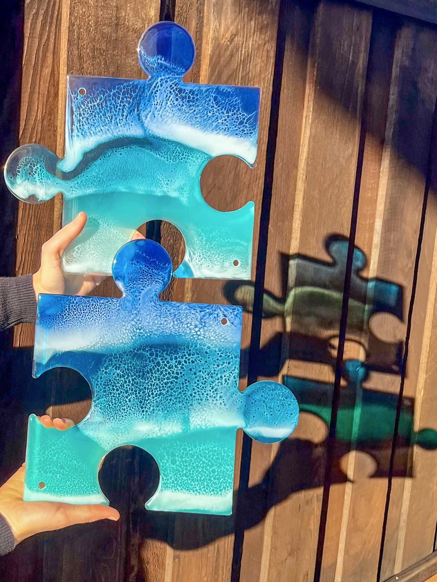 Woman holding resin ocean puzzle artwork against wall casting colorful blue shadows.