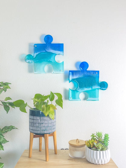 Two see-through blue puzzle pieces with resin ocean waves casting colorful shadows on wall.