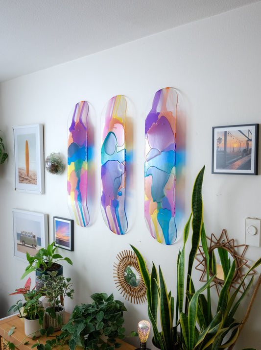 Three see-through stained glass skateboard decks with pink, purple, yellow, blue and orange resin casting colorful shadow on wall.