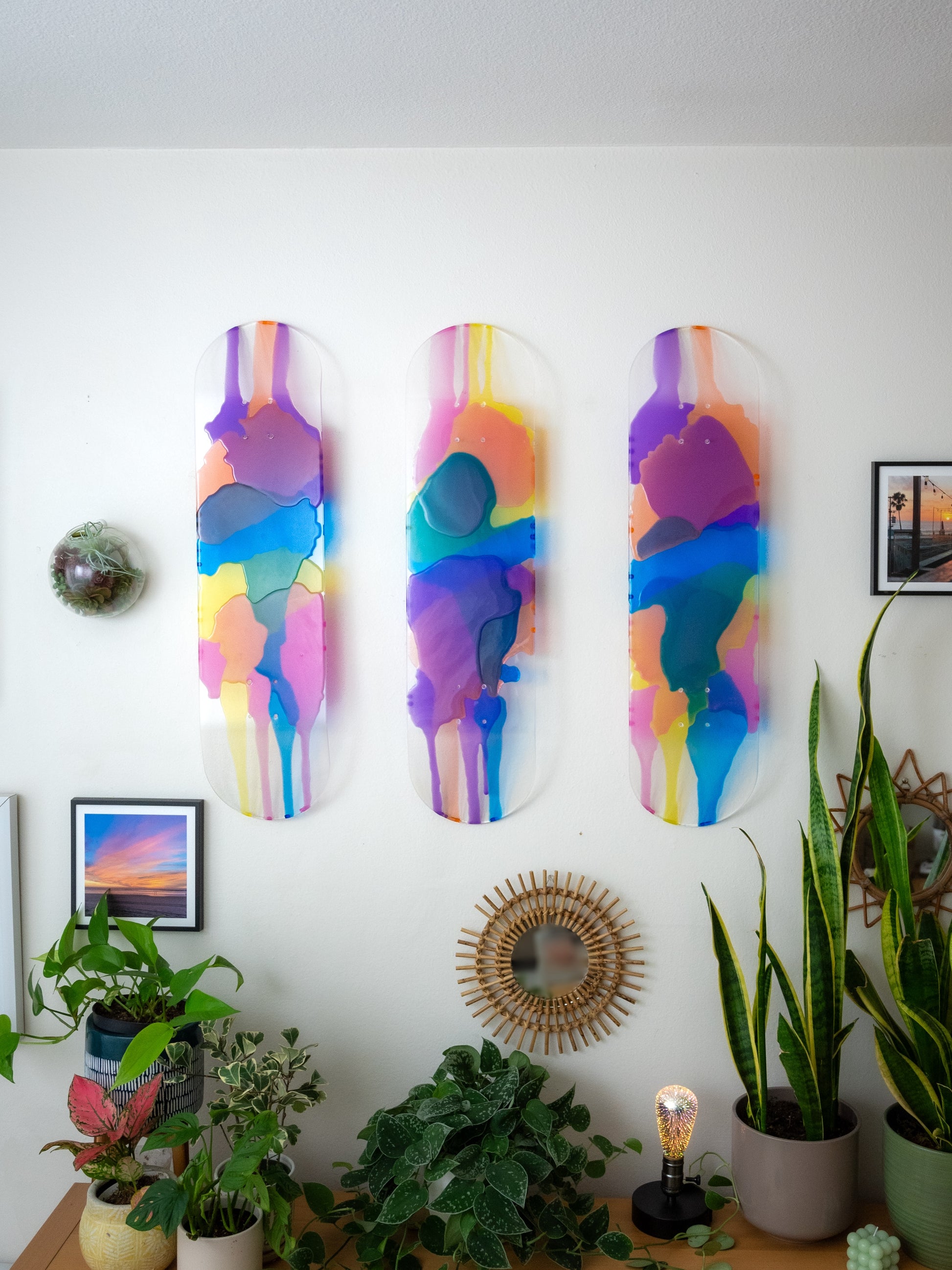 Three see-through stained glass skateboard decks with pink, purple, yellow, blue and orange resin casting colorful shadow on wall.