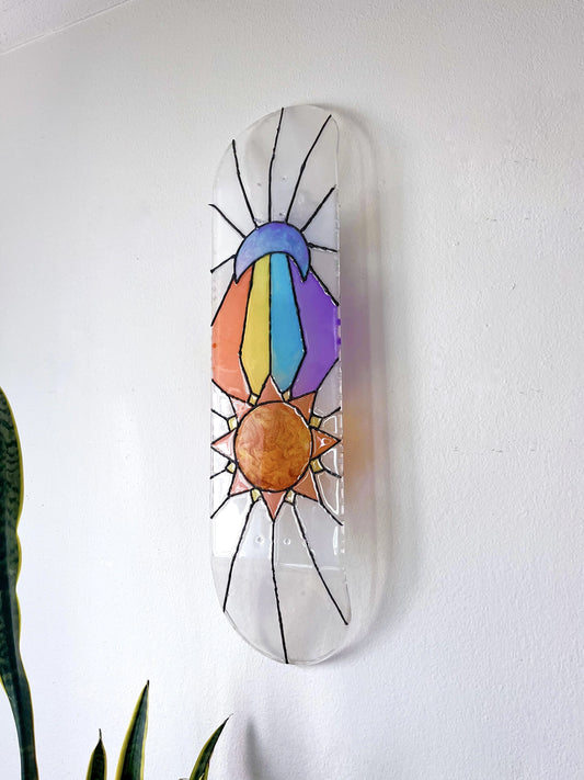 Stained glass see-through skateboard wall art featuring sun and moon design casting colorful shadow.