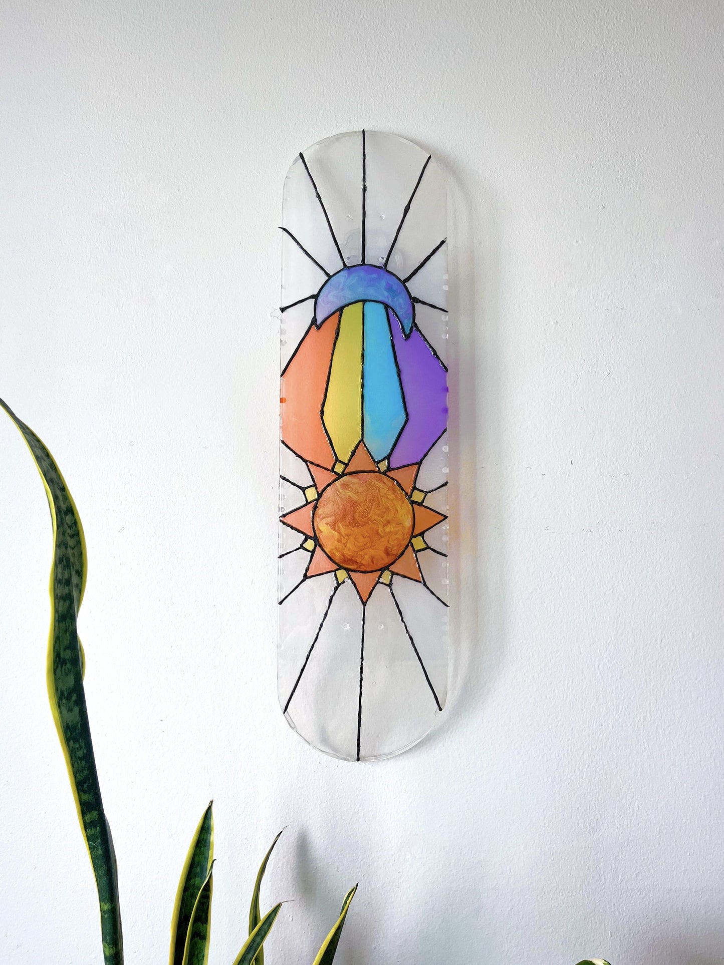Stained glass see-through skateboard wall art featuring sun and moon design casting colorful shadow.