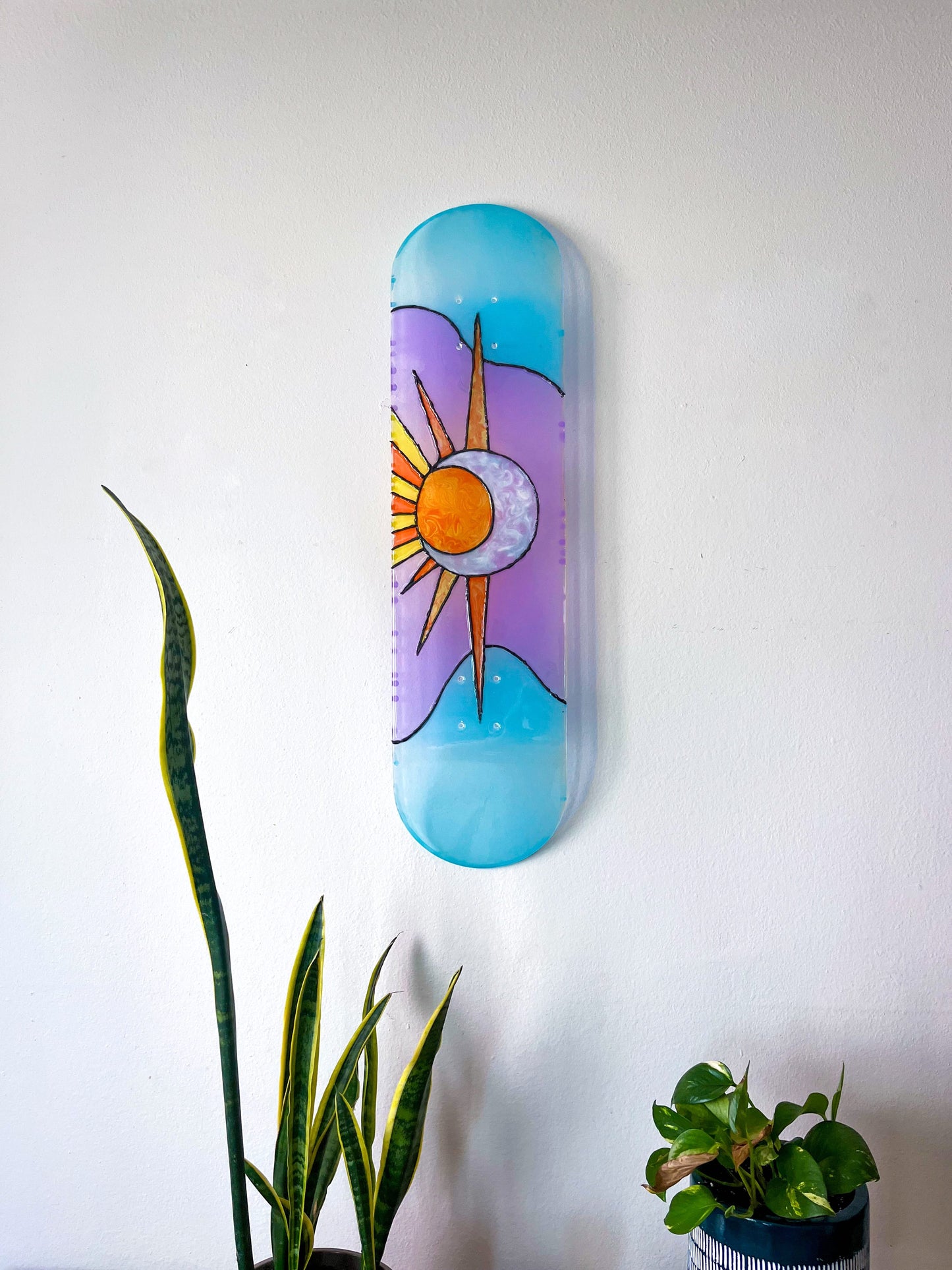 Sun and Moon stained glass resin skateboard art hanging on wall casting colorful shadow.