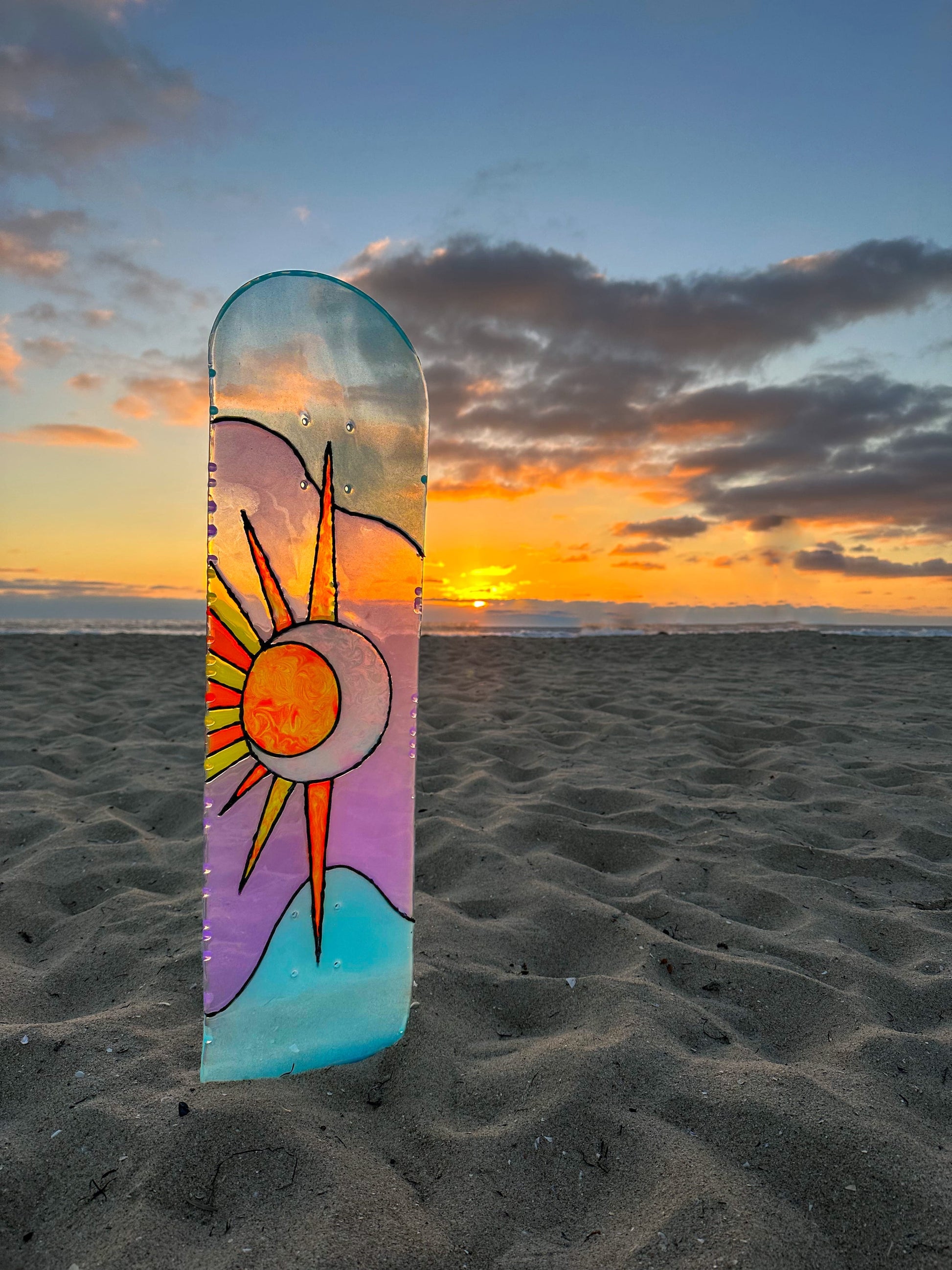 Purple and blue stained glass 'Sun and Moon' skateboard wall art at beach during sunset.