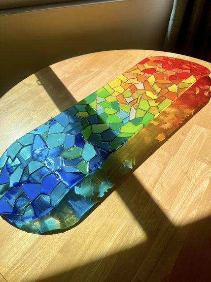 Transparent rainbow stained glass skateboard deck casting a colorful shadow.