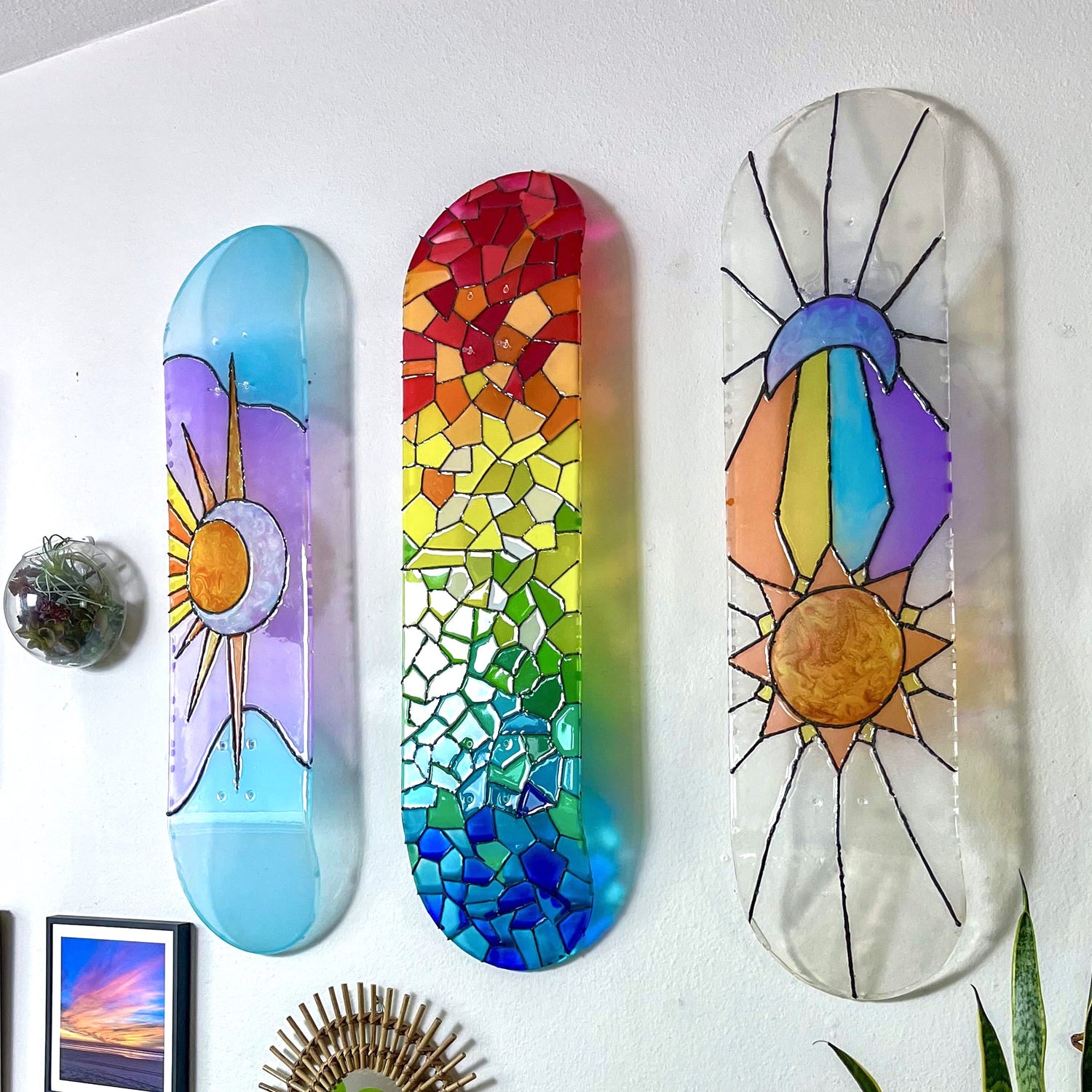 Three piece artwork of see-through stained glass resin skateboard decks hanging on wall casting colorful shadows.