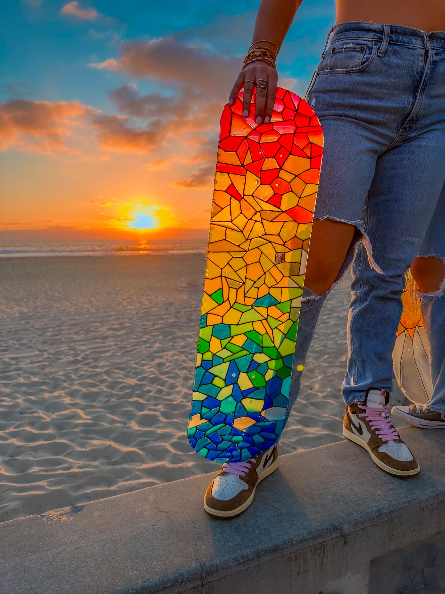 Rainbow stained glass skateboard art at beach during sunset