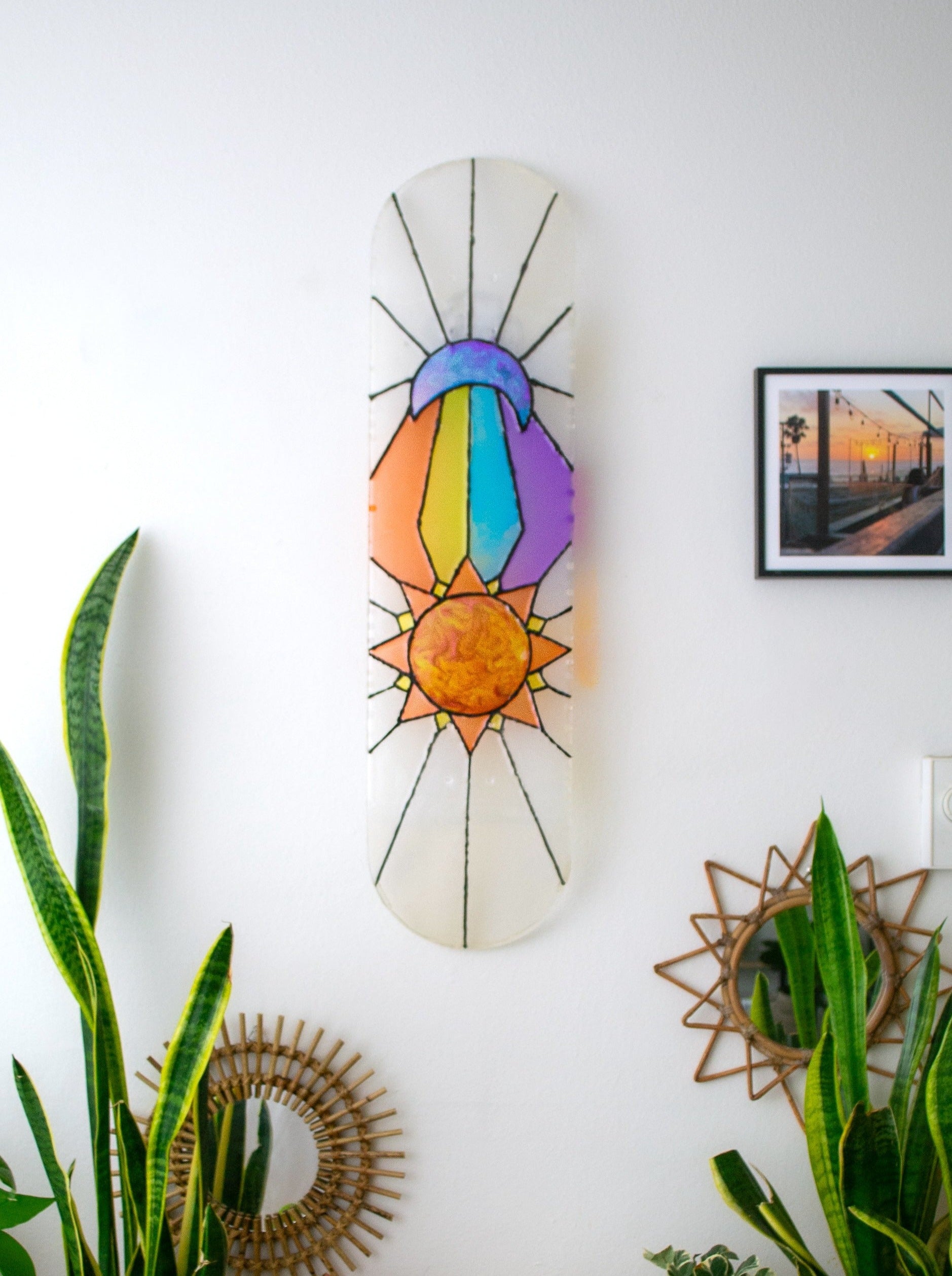 See-through, vibrant, stained glass, sun and moon resin skateboard deck wall art casting colorful shadow.