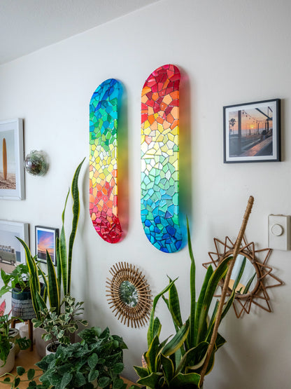 Two rainbow stained glass skateboard decks casting colorful shadows.