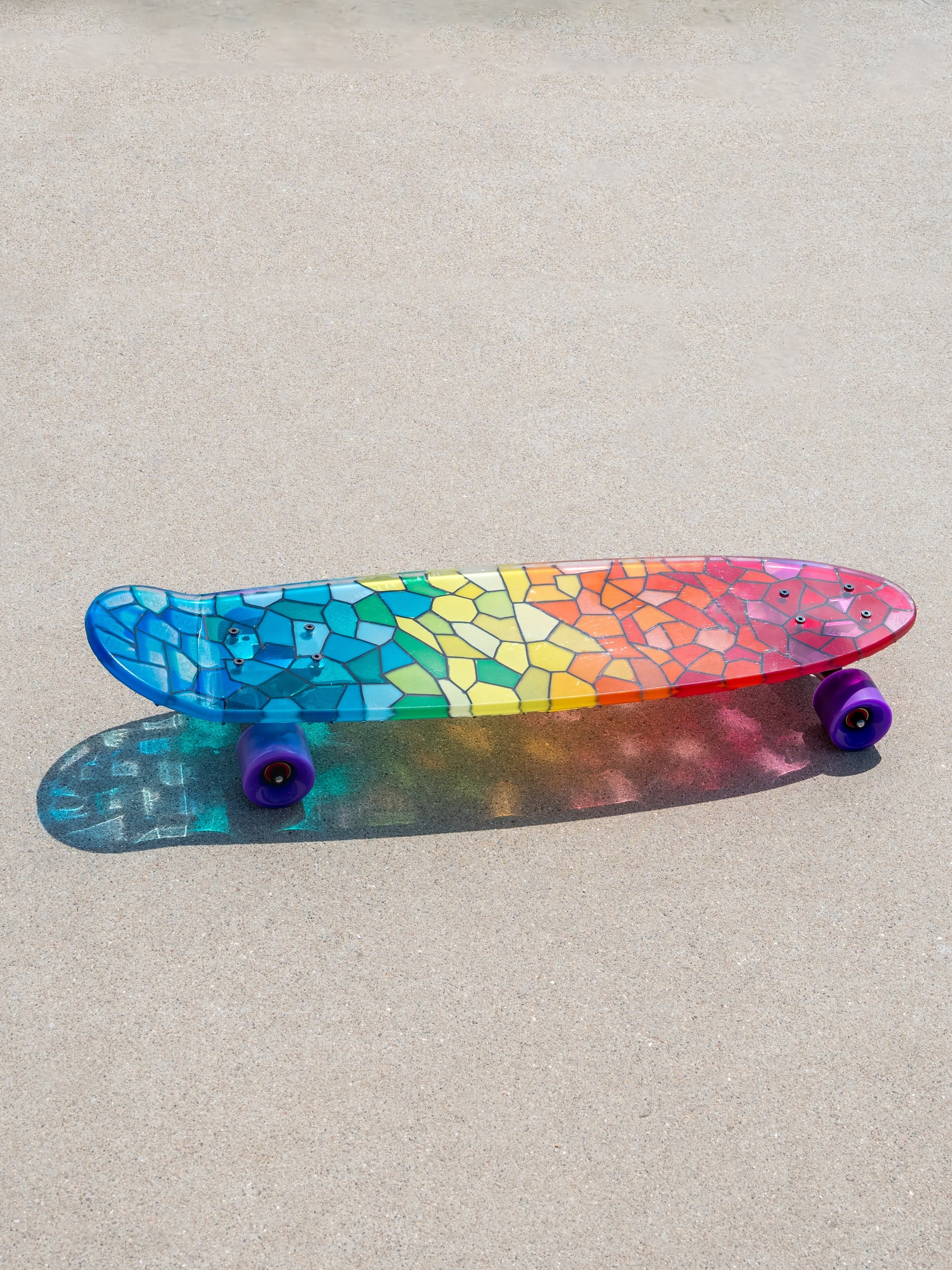 See-through rainbow stained glass skateboard with colorful shadow.
