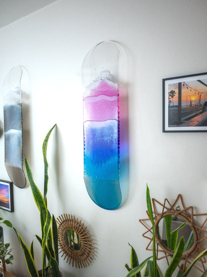 See through pink, purple, and blue ocean skateboard wall art with resin waves casting colorful shadow.