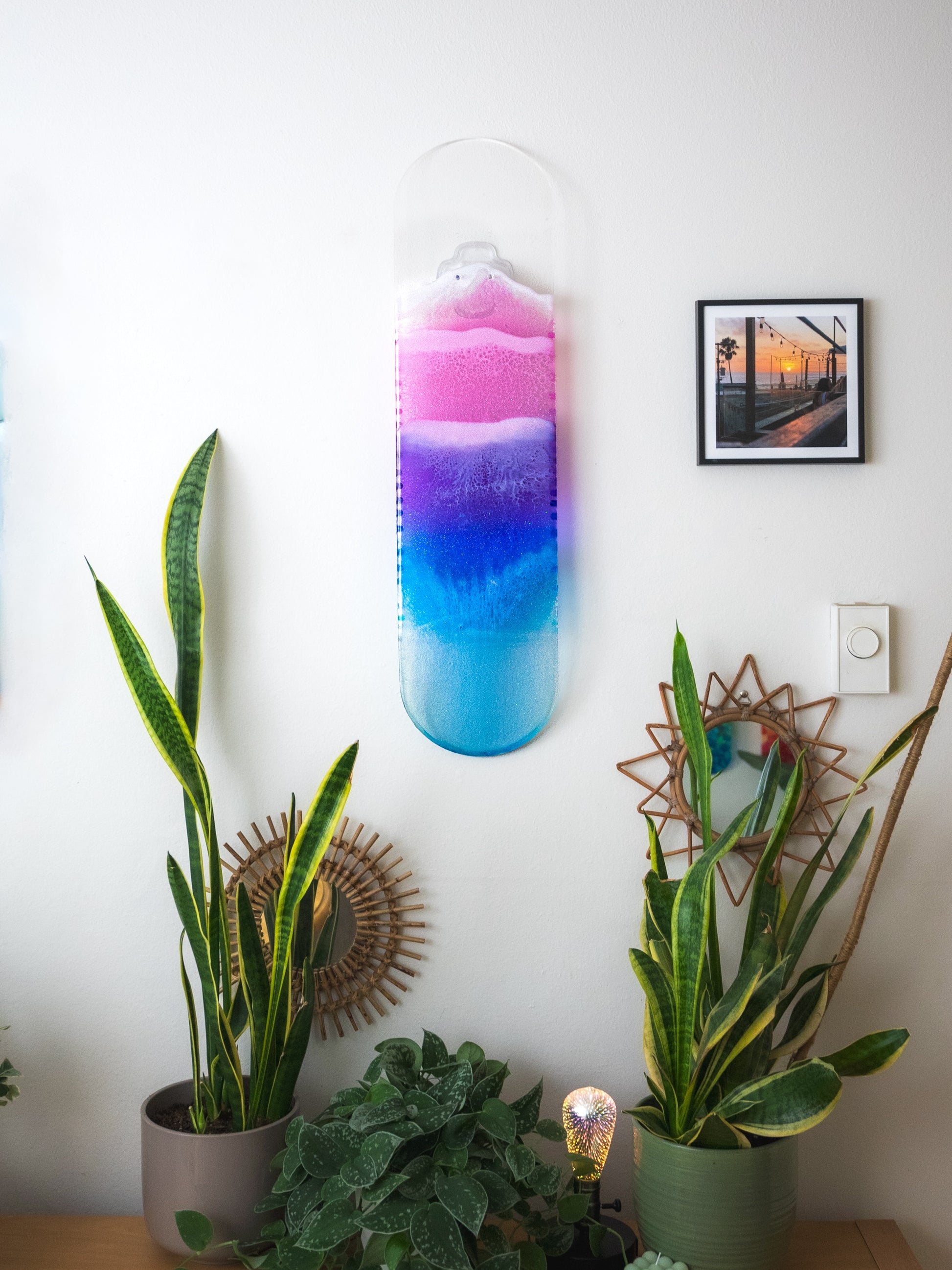 See through pink, purple, and blue ocean skateboard wall art with resin waves casting colorful shadow.