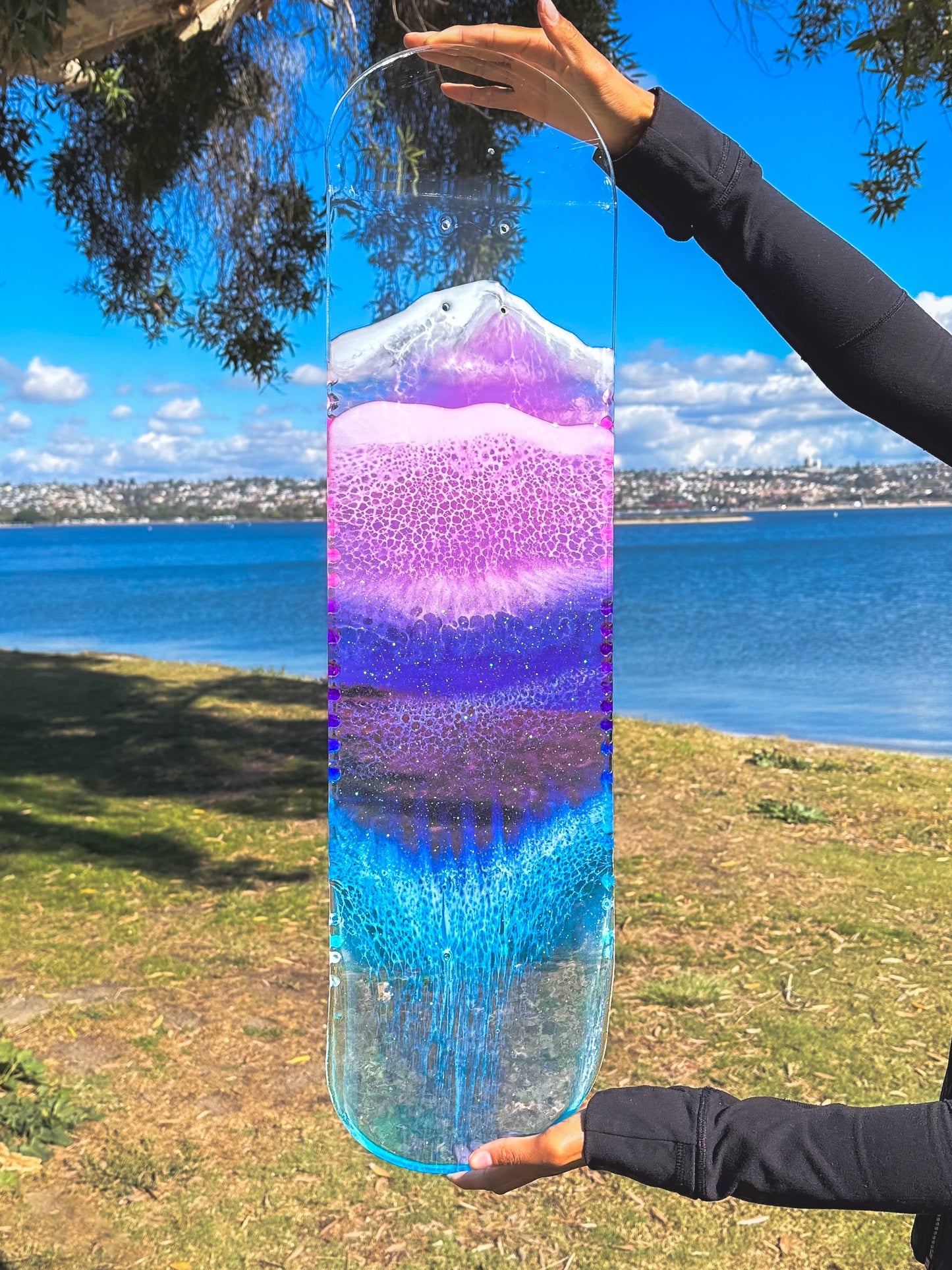 See through pink, purple, and blue ocean skateboard wall art with resin waves casting colorful shadow.