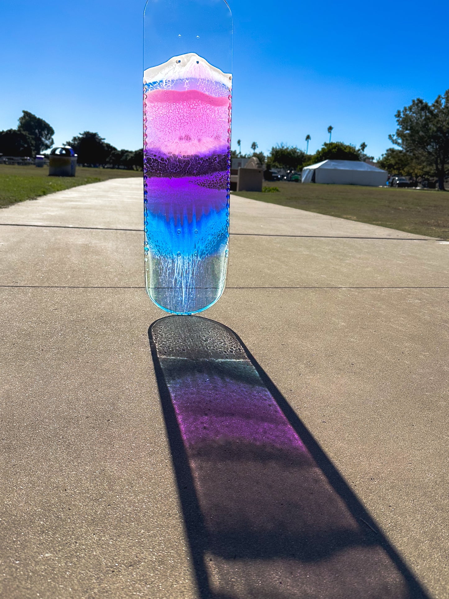 See through pink, purple, and blue ocean skateboard wall art with resin waves casting colorful shadow.