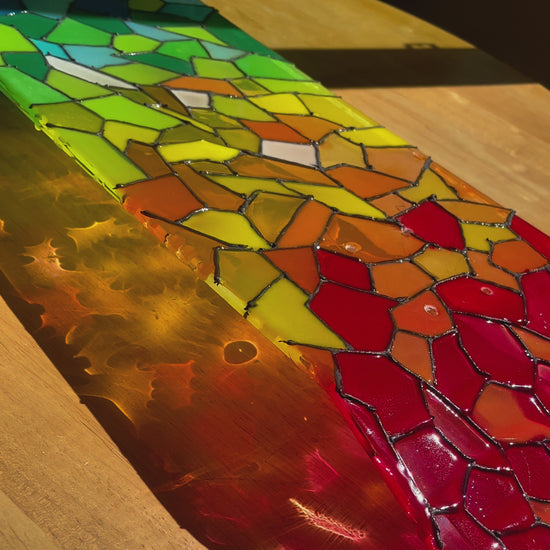 See-through rainbow stained glass skateboard deck casting a colorful shadow.