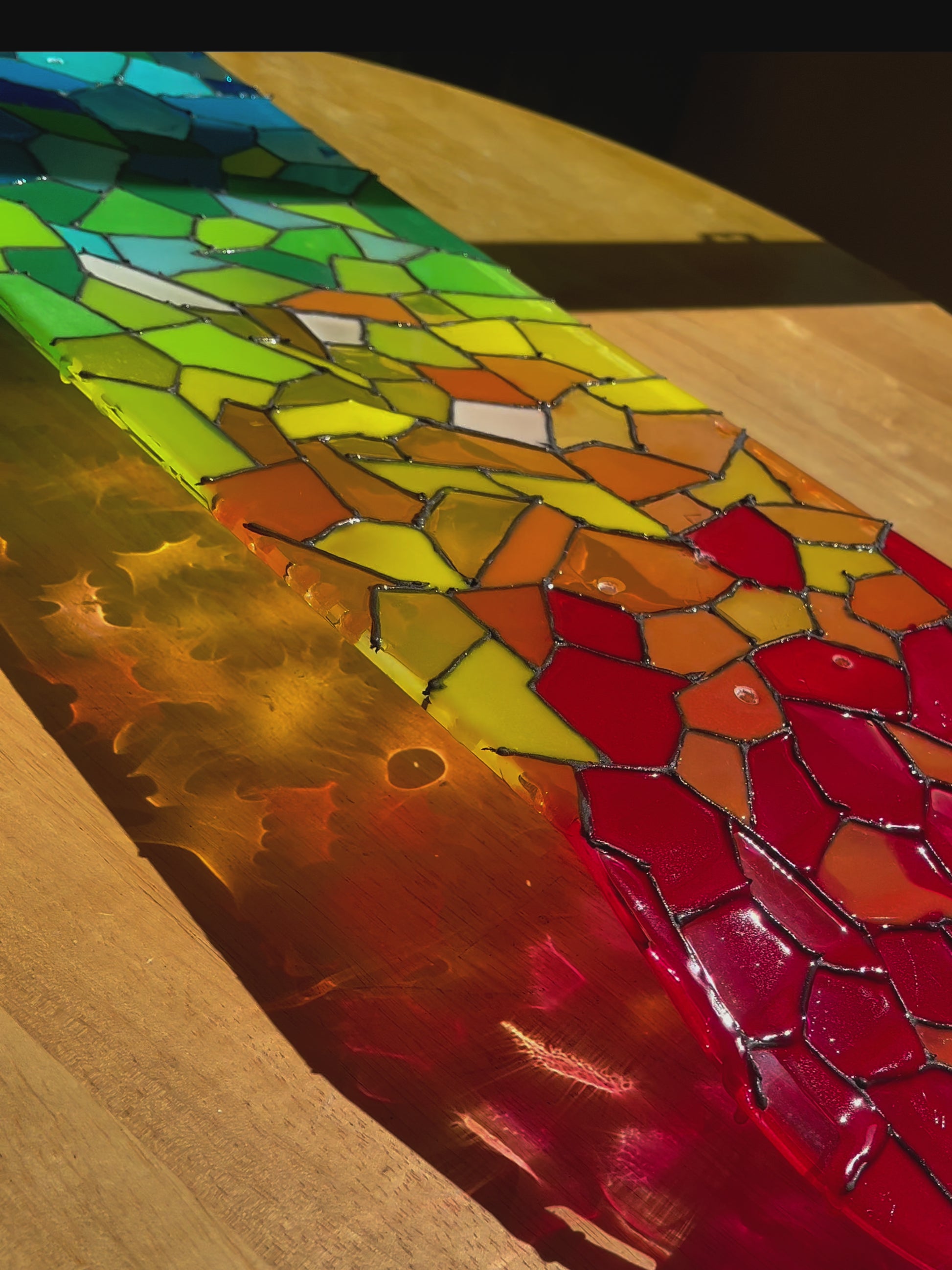 See-through rainbow stained glass skateboard deck casting a colorful shadow.